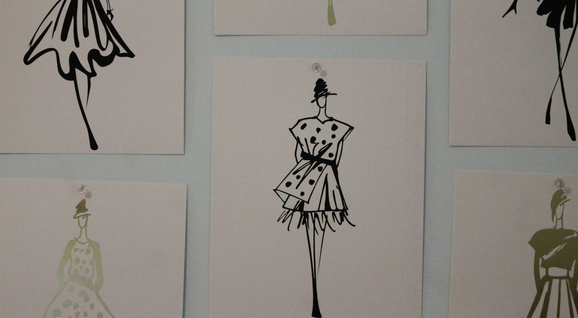Fashion illustrations of dresses and outfits pinned to a wall, representing fashion design, creativity and collection development.