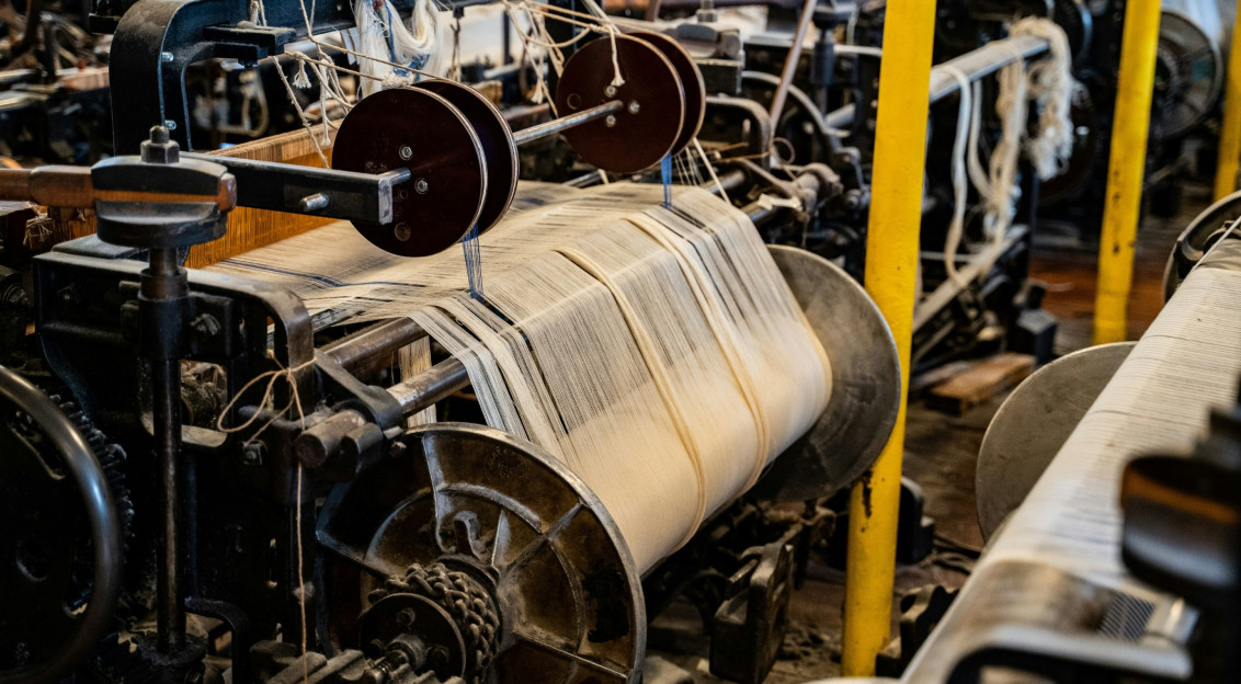 Industrial weaving machinery processing yarn in a textile production facility.