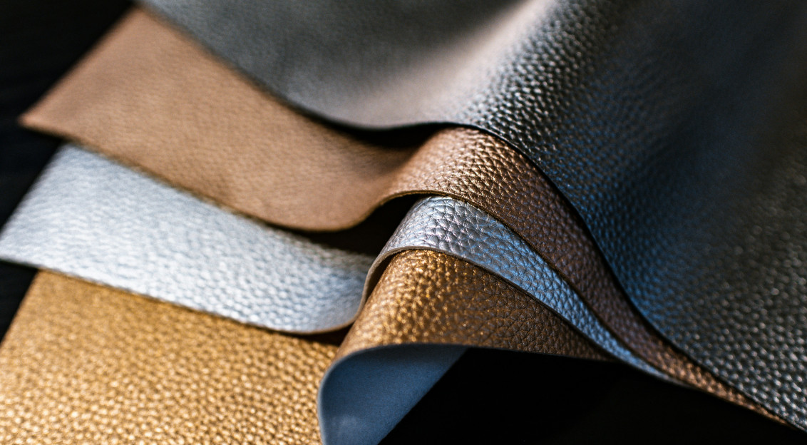Close-up of layered textured material samples in metallic gold, silver, bronze and black tones, representing innovative material development and textile design.