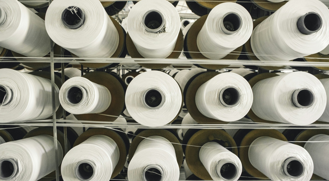 Rows of large white yarn cones stored on racks in a textile production facility.