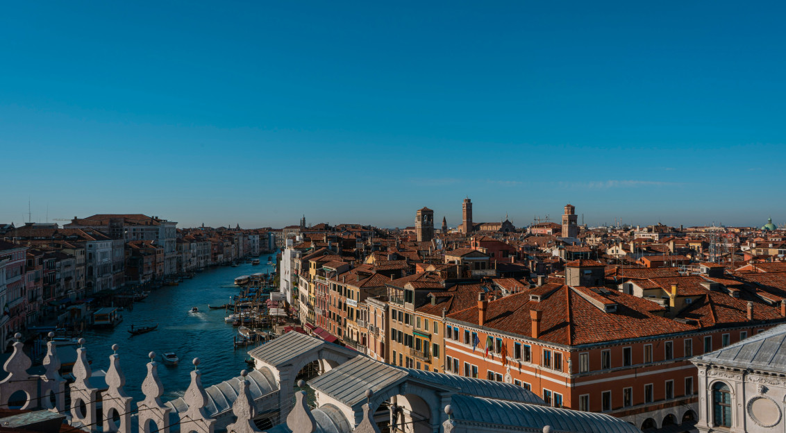Aerial view of Venice, Italy, showing the Grand Canal winding between historic buildings and the Rialto Bridge. 
