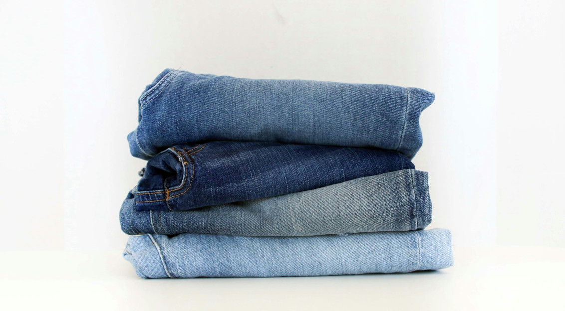 Stack of folded blue jeans in different denim washes, ranging from light to dark blue