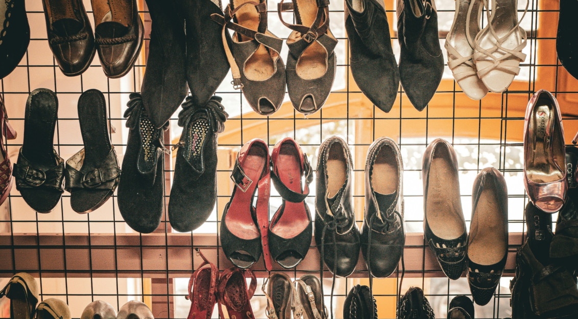 Various styles of women's footwear, including boots, sandals, heels and leather shoes, displayed on a metal rack in a retail setting.