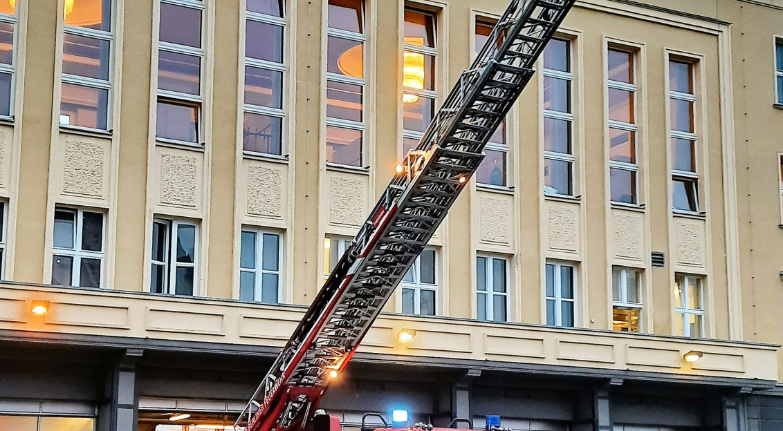 This picture shows a firefighting ladder truck positioned outside a large building, with its telescopic aerial ladder fully extended toward the upper floors.