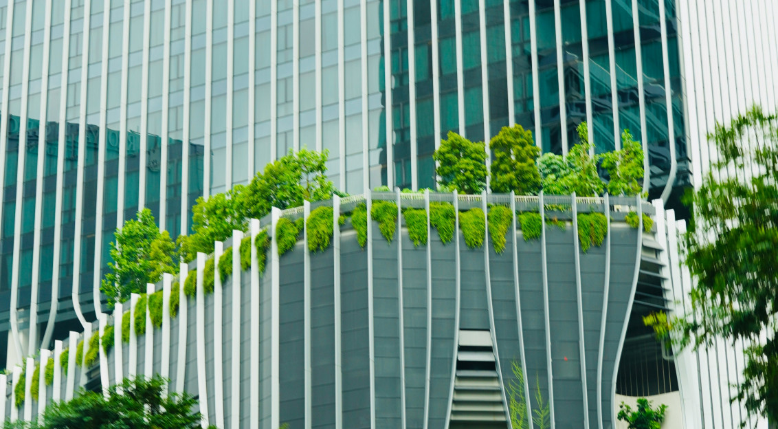 The picture shows a modern building with glass façades, distinctive white structural elements, and lush greenery integrated across terraces and balconies.