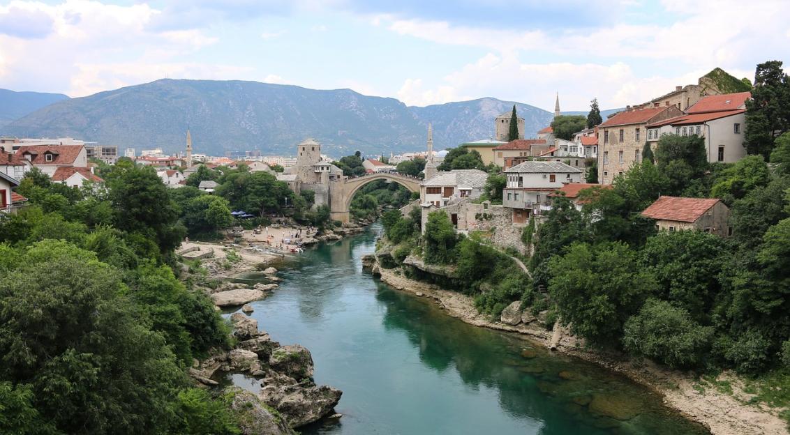 An illustrative photo of a river between coasts with houses and with mountains in the background
