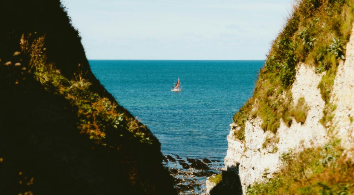 An illustrative photo of a boat in the water near a cliff.