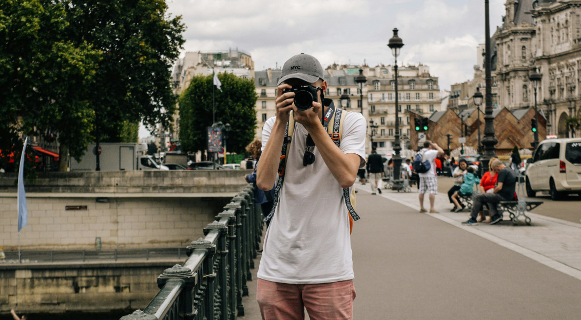An illustrative photo of a man holding a camera while standing on a bridge