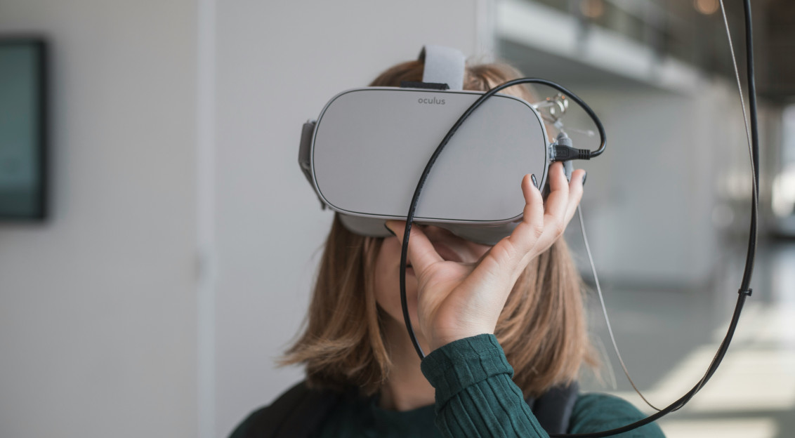 An illustrative photo of a woman holding white and black VR goggles.
