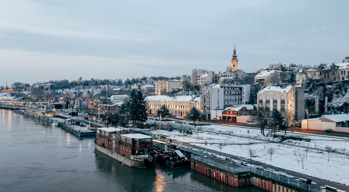 An illustrative photo of city buildings covered in snow near a body of water.