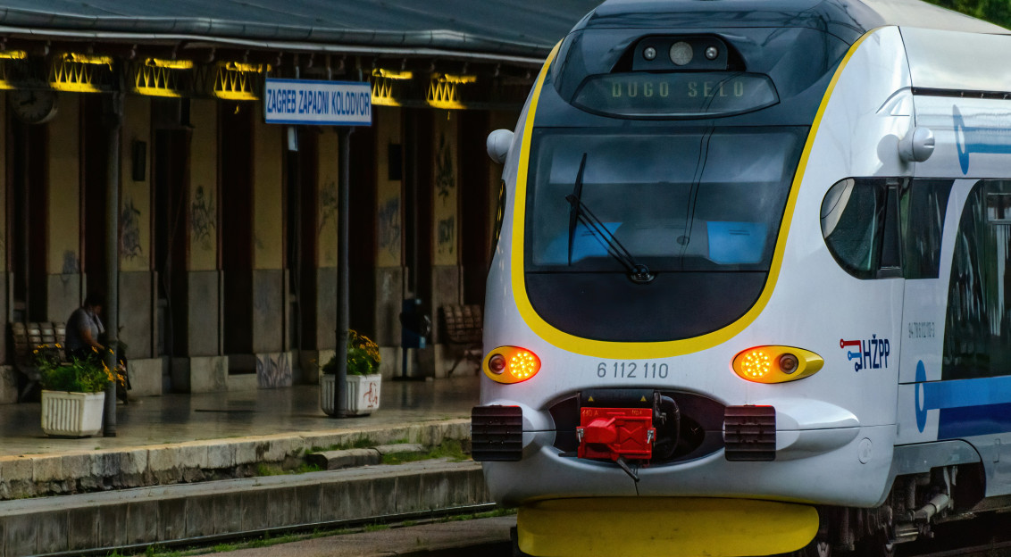 Image by Unsplash An illustrative photo of a white and blue train traveling past a train station.