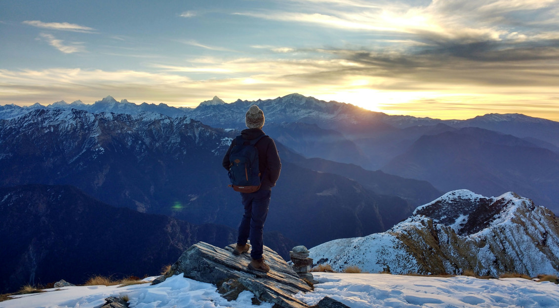 An illustrative photo of person standing on top of the mountain facing sunrise.