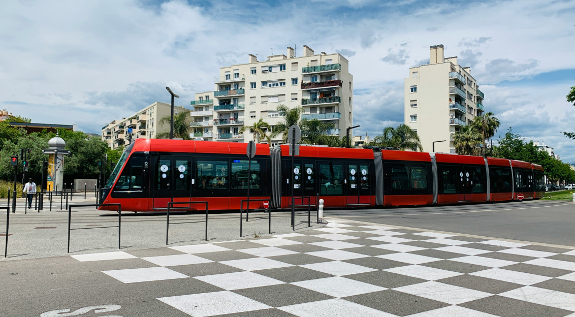 An illustrative photo of a red and black train traveling past tall buildings.