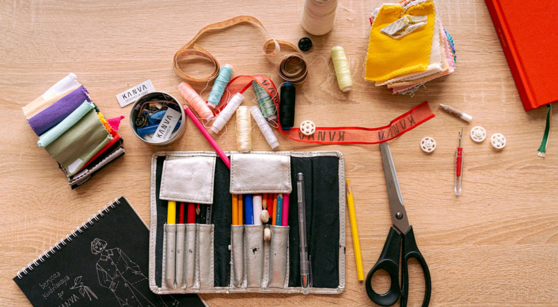 A neatly arranged workspace with sewing tools, fabric swatches, threads, scissors, and a sketchbook.