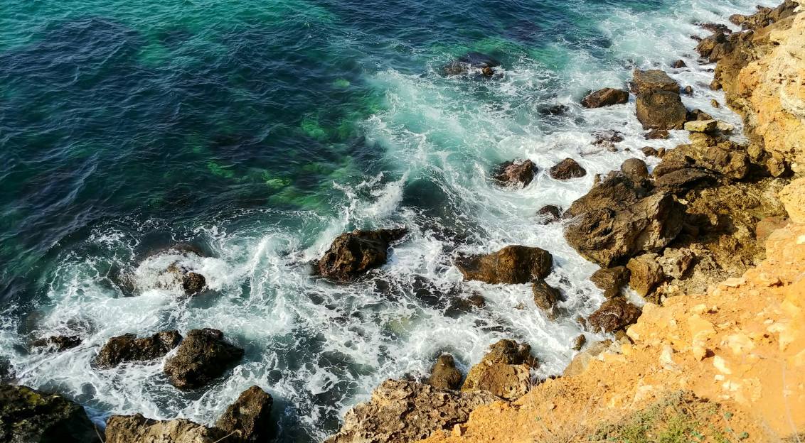 An illustrative photo of brown rocky shore with blue sea water during daytime.