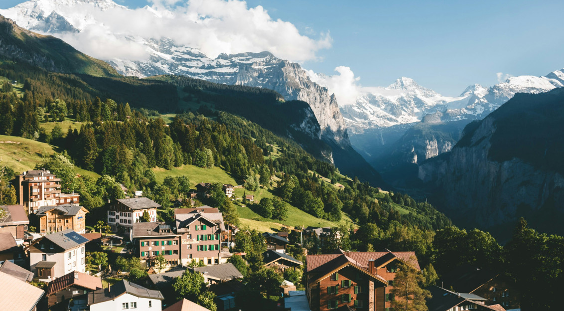 Image by Unsplash An illustrative photo of brown and white houses on green mountain under blue sky.