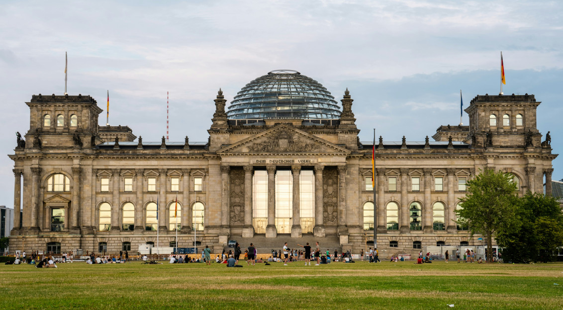 An illustrative photo of people sitting on grass near a large building with a dome.