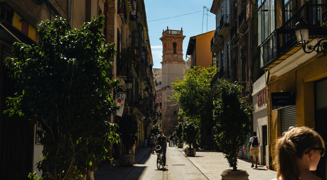 An illustrative photo of a man riding a bicycle on a narrow street surrounded by buildings.