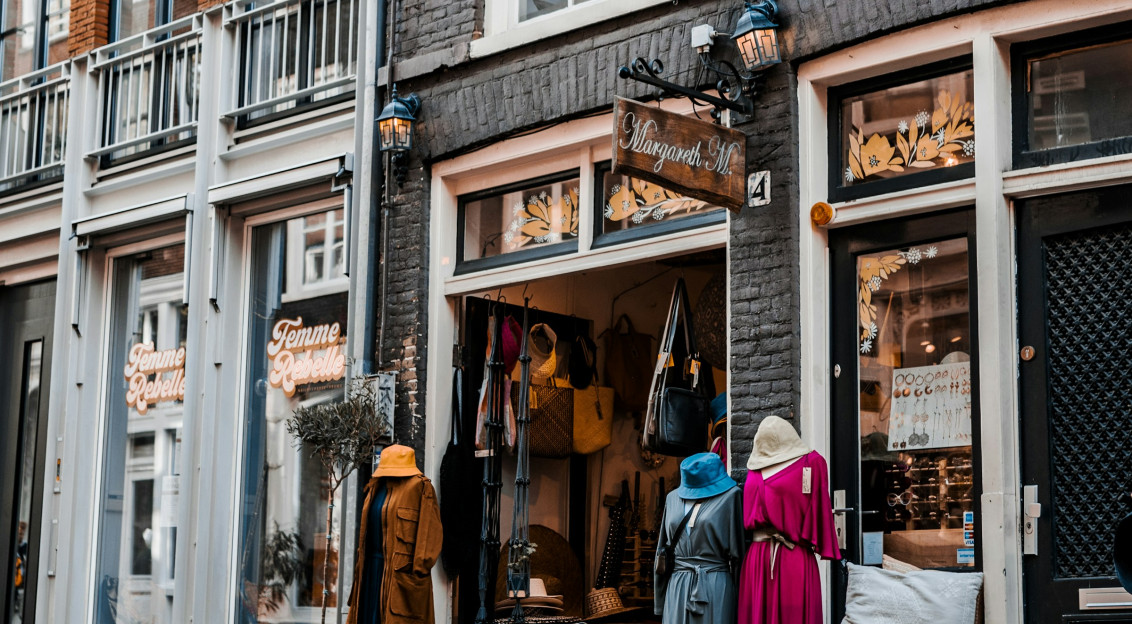 Street view of a small clothing boutique with dresses displayed outside.