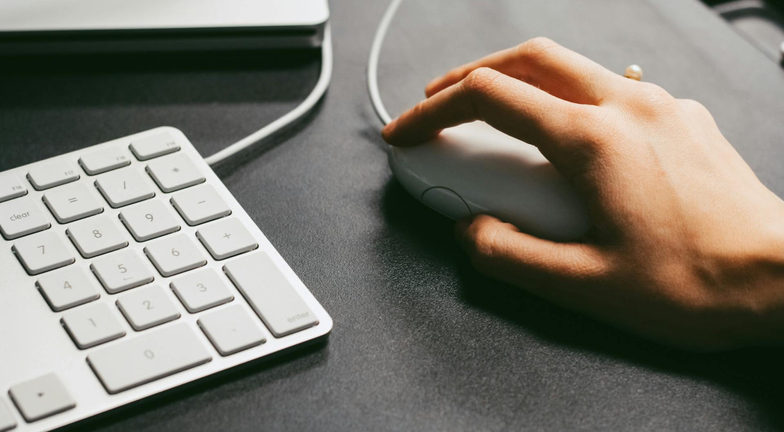 Hand using a computer mouse beside a keyboard on a desk.