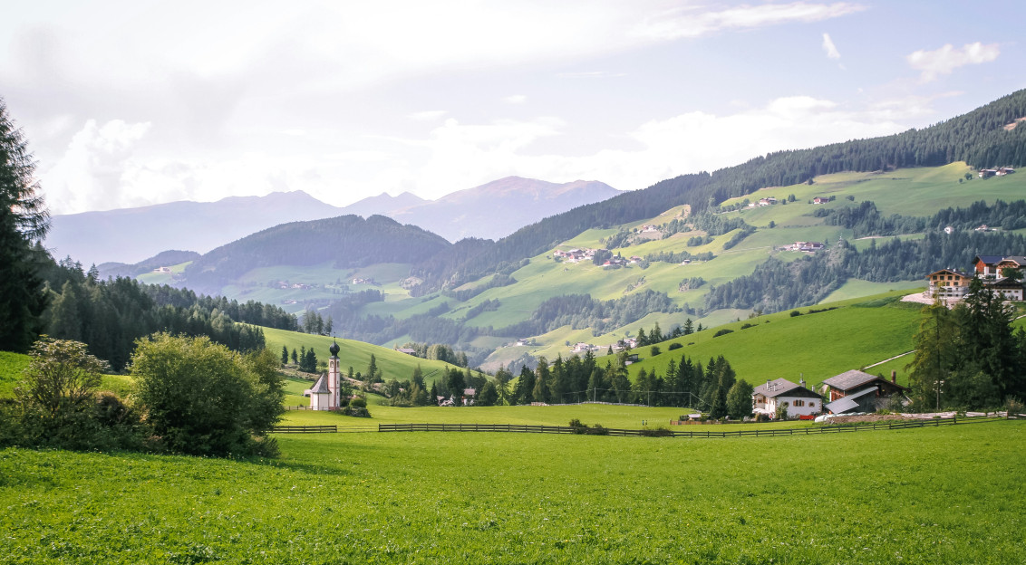 An illustrative photo of a green grass field near green mountains.