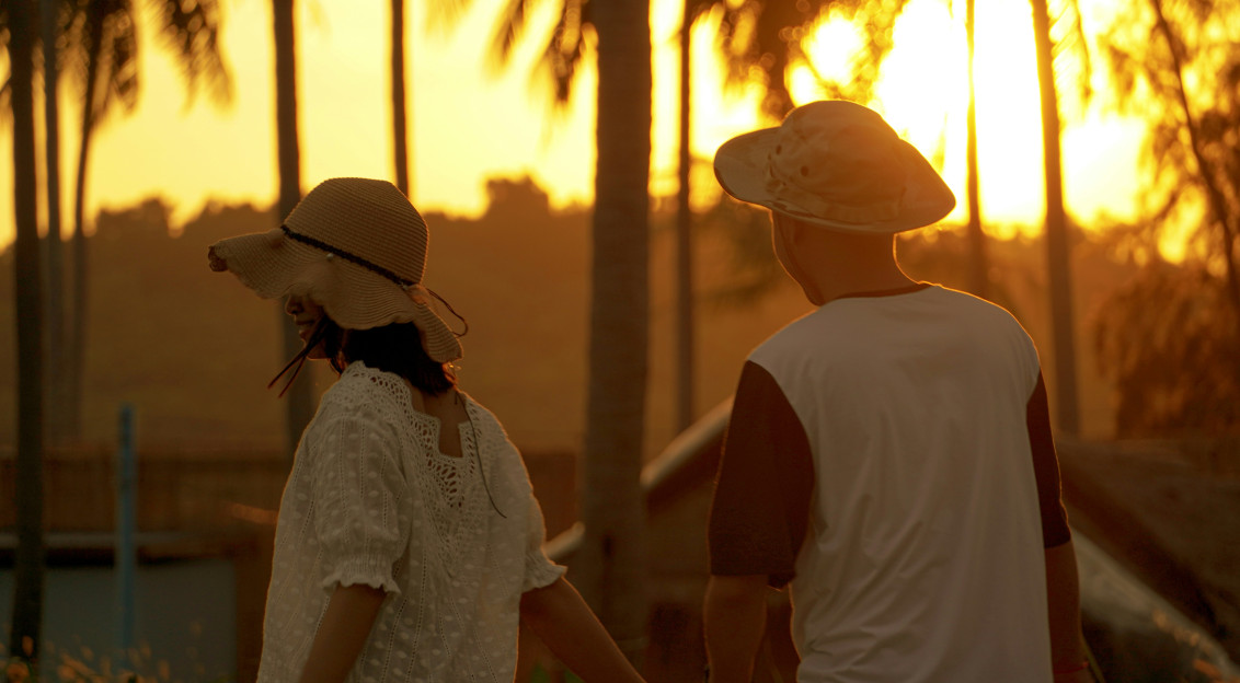 An illustrative photo of a man and a woman holding hands in front of a sunset.