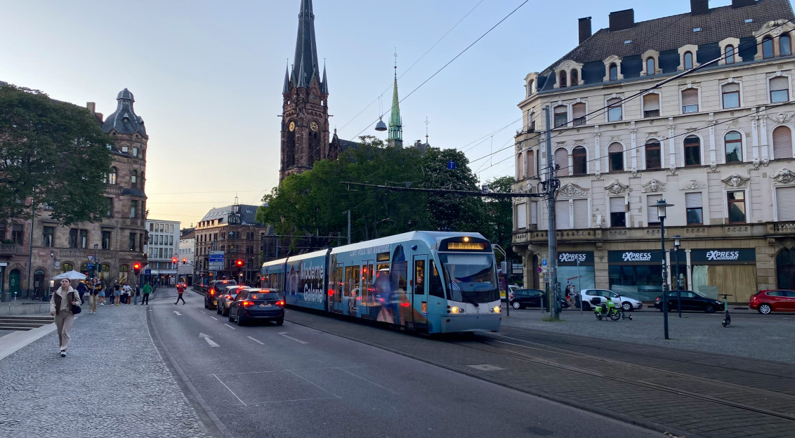 An illustrative photo of a blue and white train traveling down a street next to tall buildings.