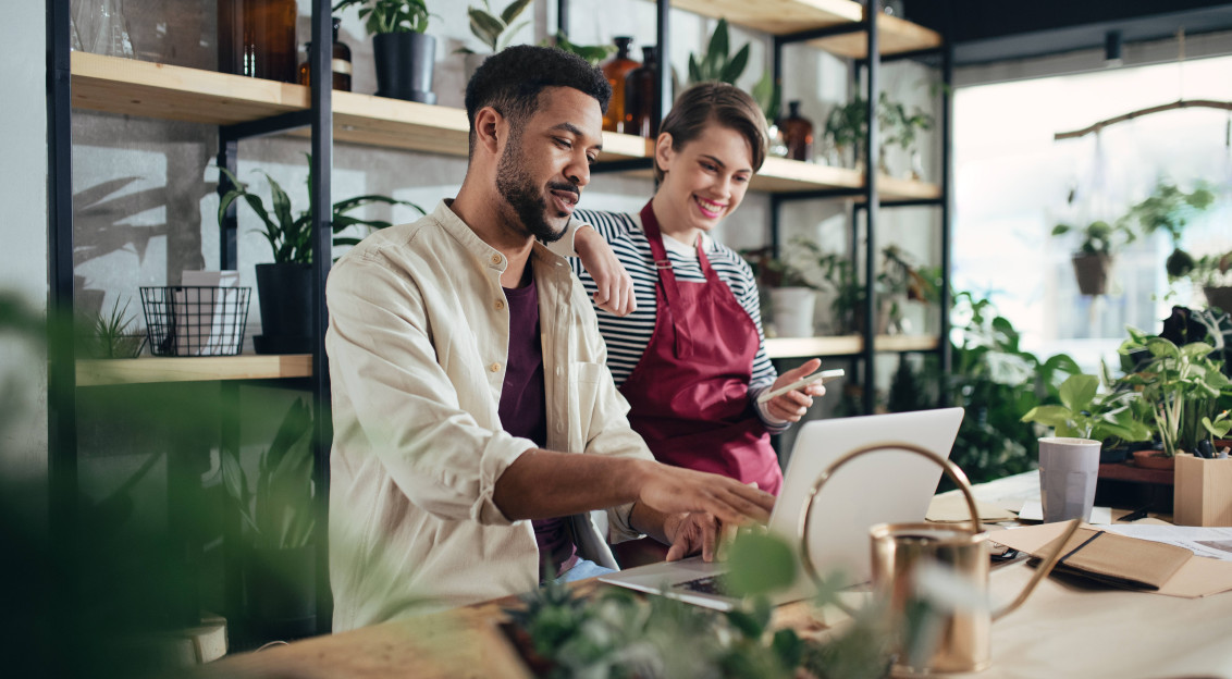 A photo presenting two people working together on a laptop in a plant-filled shop.
