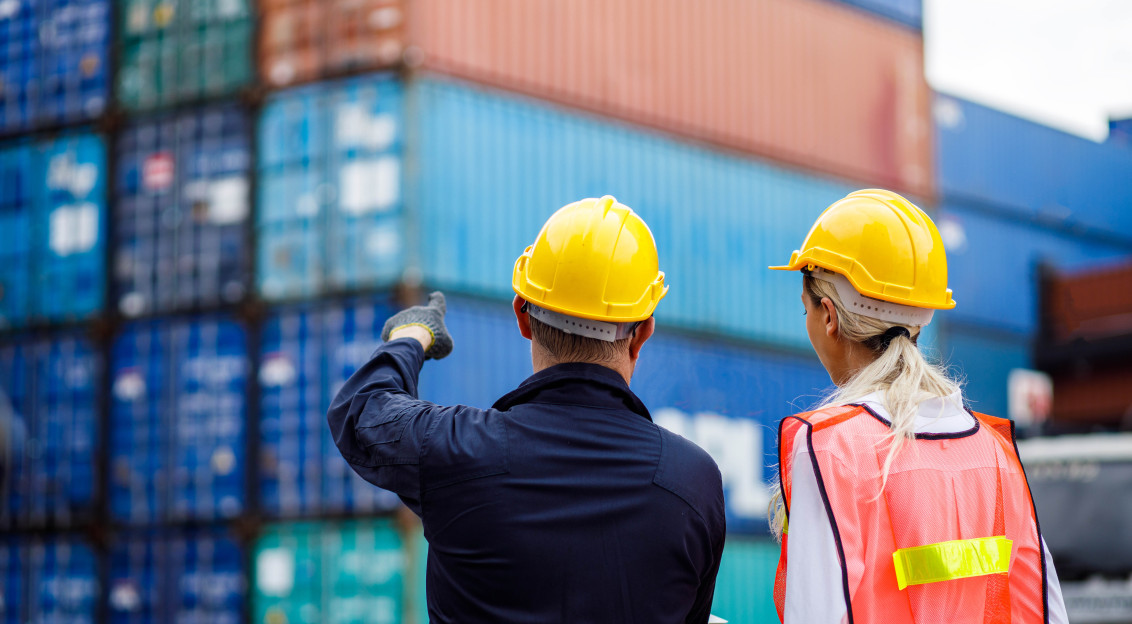 A photo presenting two workers in safety helmets inspecting stacked shipping containers at a cargo terminal.