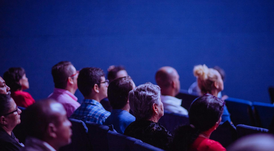 Audience seated and watching a presentation in a darkened conference or auditorium.