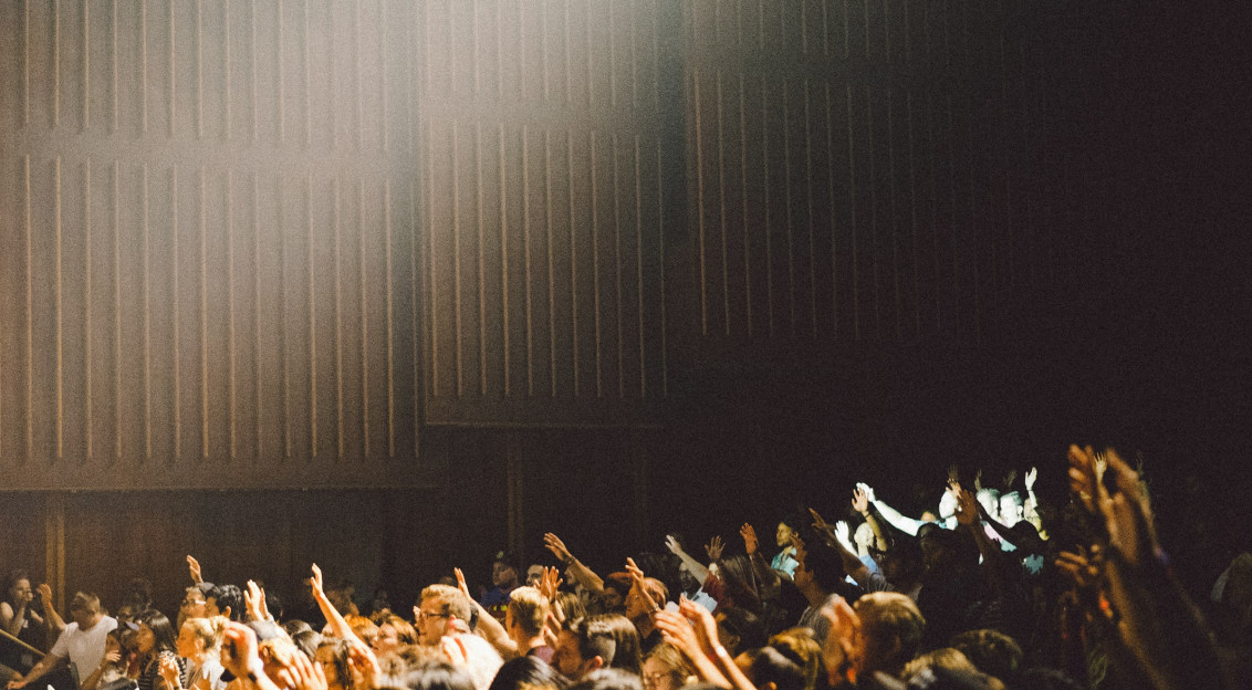 Participants with raised hands at a live event, lit in a dark indoor venue.