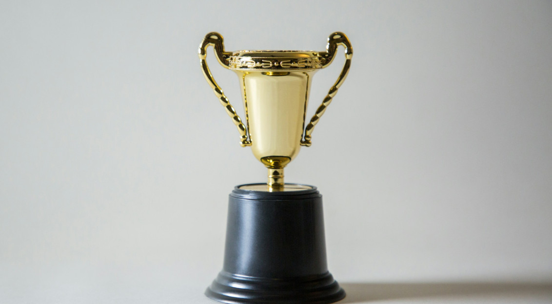 Gold trophy cup with handles on a black base against a plain background.