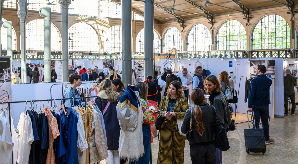 Indoor fashion exhibition with clothing racks and attendees browsing.