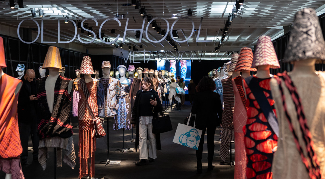 Visitors walking through a textile exhibition space featuring mannequins dressed in innovative knitwear designs and materials.